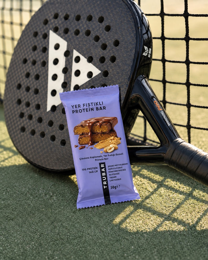 Padel raketinin yanında TRUBAR Yer Fıstıklı Protein Bar paketi