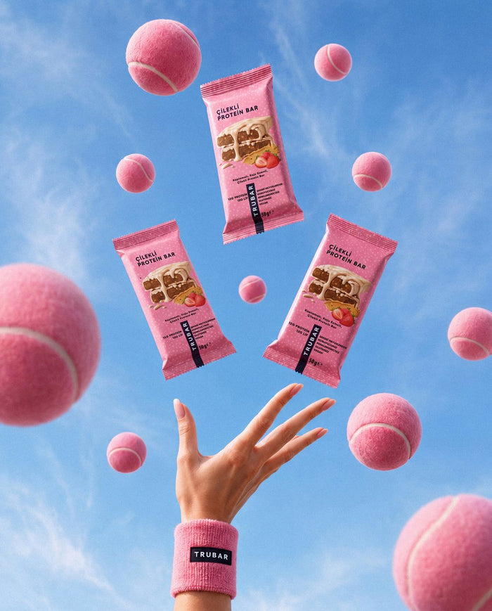 Pembe tenis topları arasında havaya atılan TRUBAR Çilekli Protein Bar paketleri